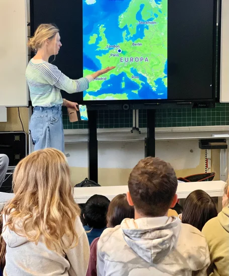 Die Klassenlehrerin zeigt auf eine Europakarte mit Paris in der Klasse